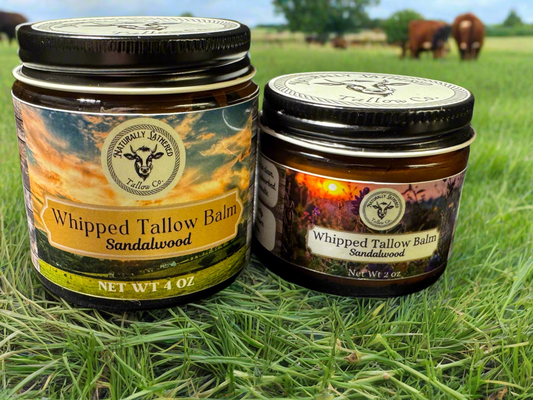 Two jars of Whipped Tallow Balm with Sandalwood scent, set in a field with horses in the background. One larger jar and one smaller jar.