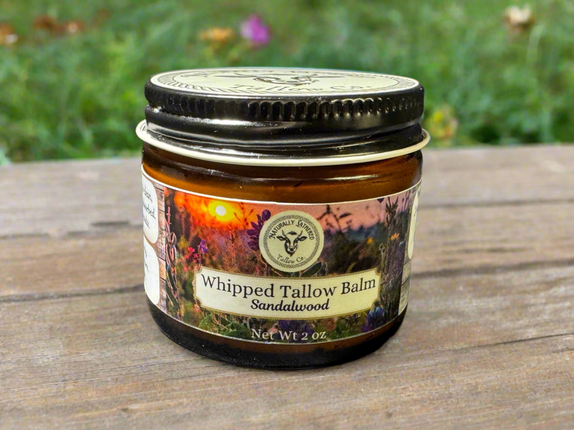 Two jars of Whipped Tallow Balm with Sandalwood scent, set in a field with horses in the background. One larger jar and one smaller jar.