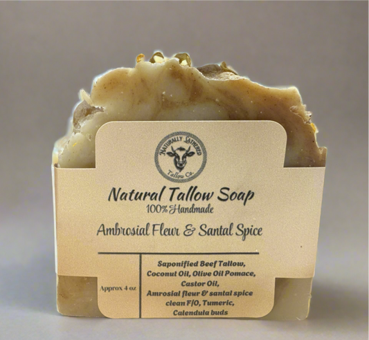 A bar of soap with a beige color and a textured surface, packaged in a brown cardboard box with a label that reads 'Natural Tallow Soap. 100% Handmade.