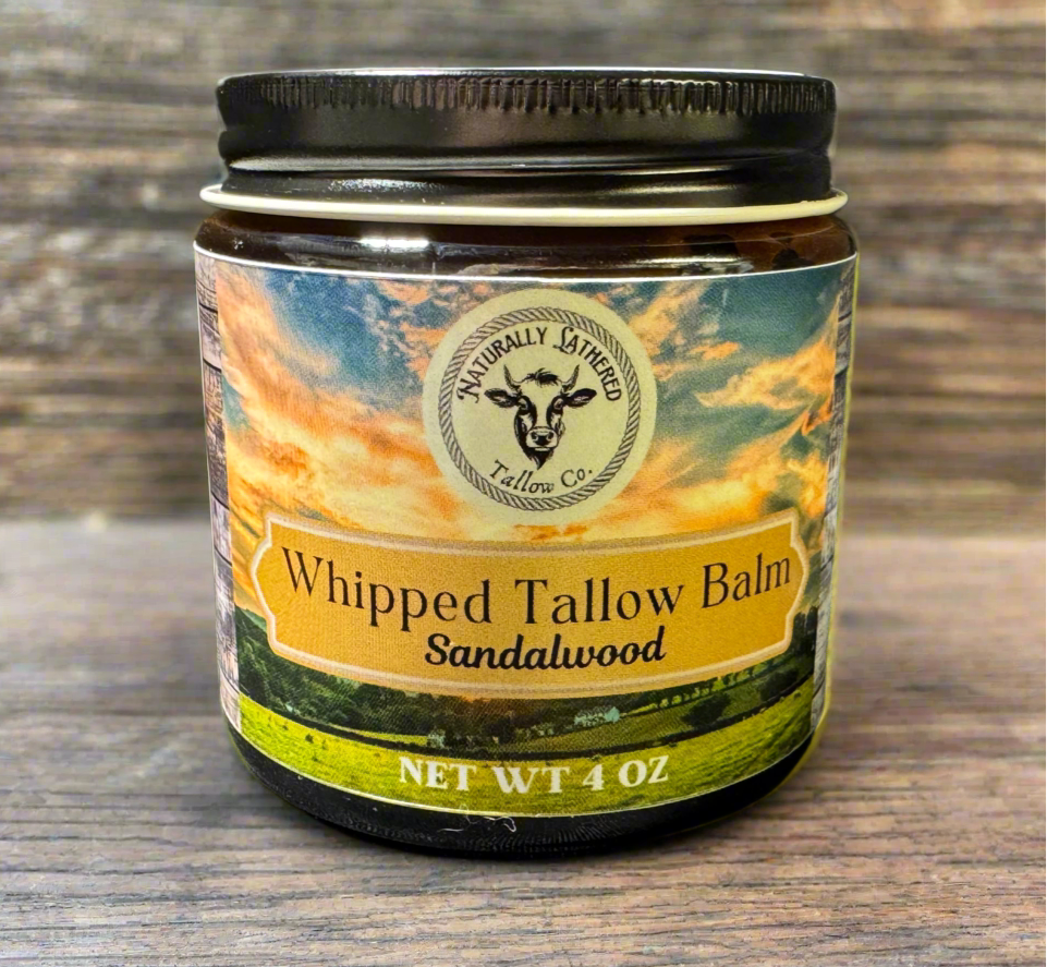Two jars of Whipped Tallow Balm with Sandalwood scent, set in a field with horses in the background. One larger jar and one smaller jar.