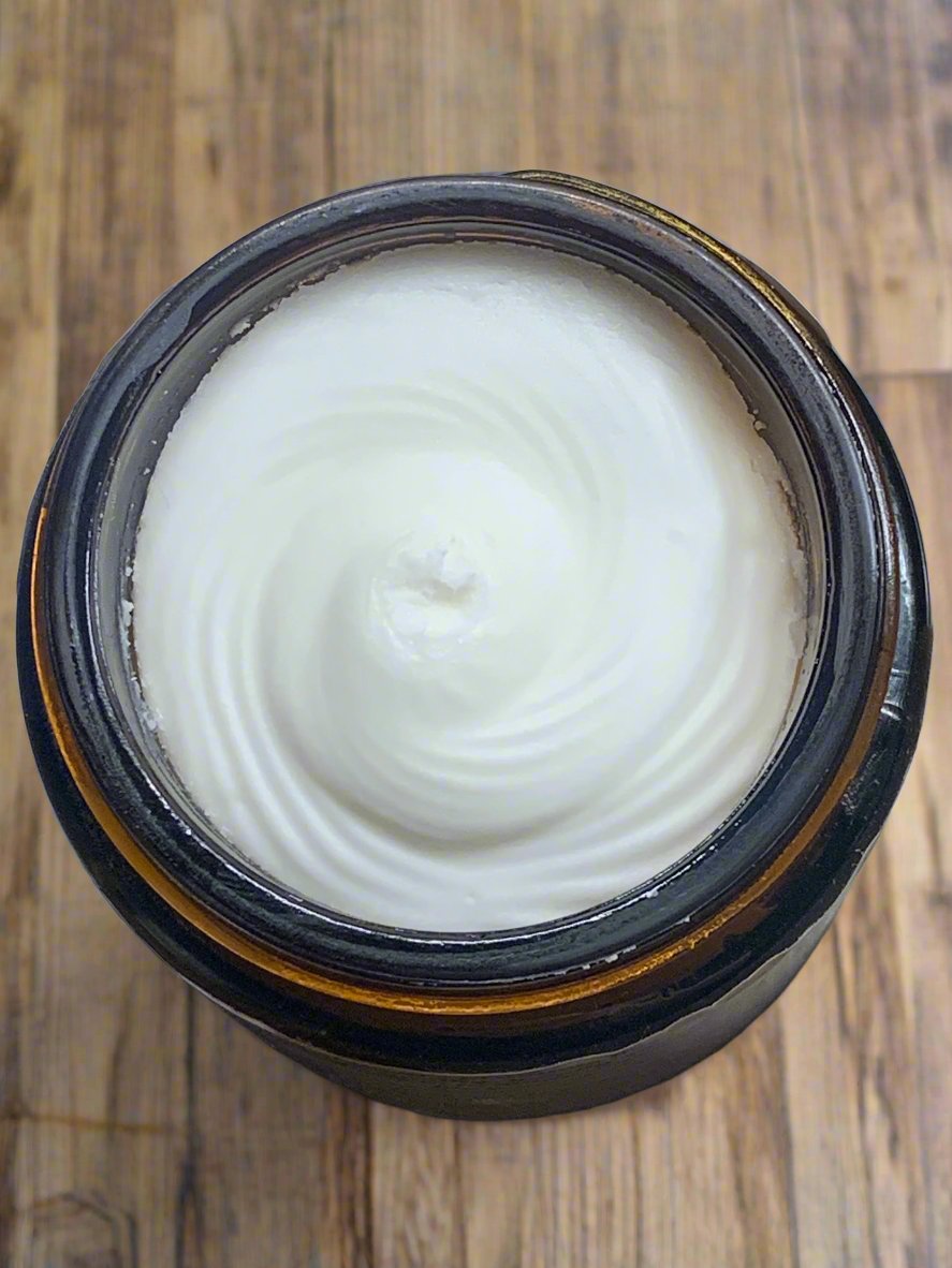 A jar of whipped tallow balm with a creamy texture, placed on a wooden surface.