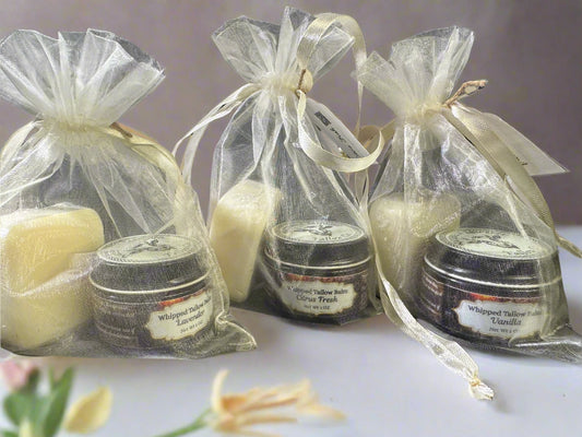 The image displays several clear organza bags with drawstrings, each containing different items including a white bar of soap and jars of balm. They are tied with beige ribbons, presenting a neat and appealing appearance.