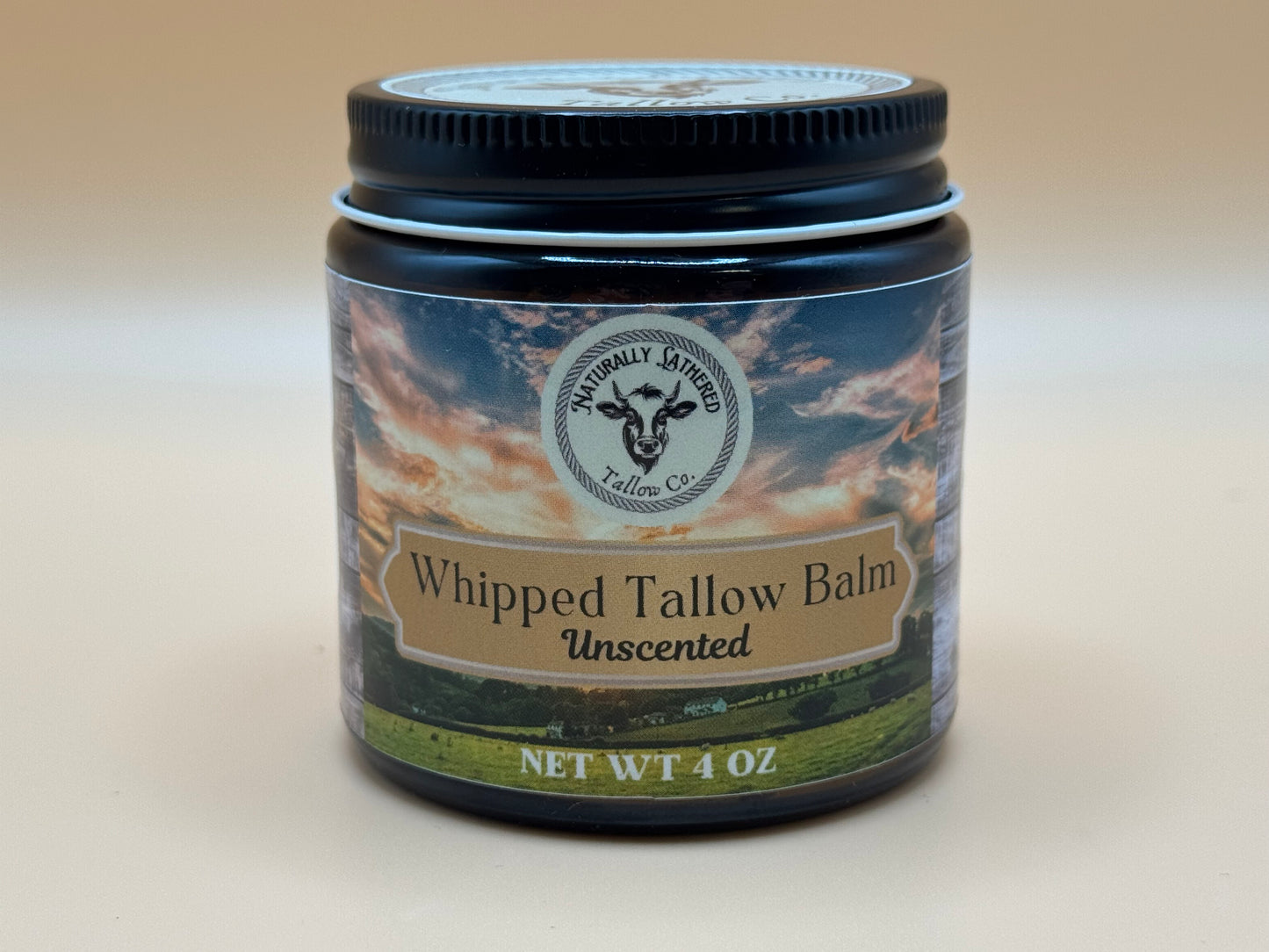 Jar of whipped tallow balm with a scenic label on a beige background